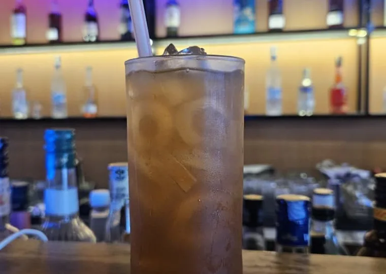 Tall iced highball drink on the bar counter, neon backlit bottle shelf behind