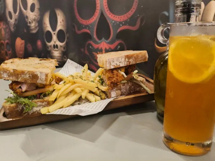 Stacked club sandwich with fries and a golden iced drink on the table